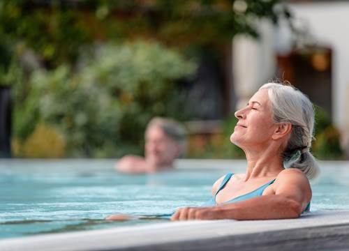 Frau am Beckenrand eines Outdoorpools genießt die Sonne