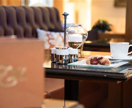 Mehlspeise, Kaffeetasse und Gedeck auf einem Tisch im Detail